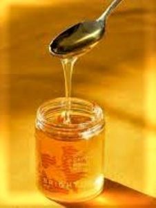 A honey jar with a spoon dripping with honey into it