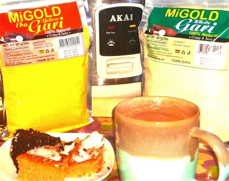 A slice of Gari sponge cake with a cup of cocoa drink in between two packets of MiGold Gari on a table.