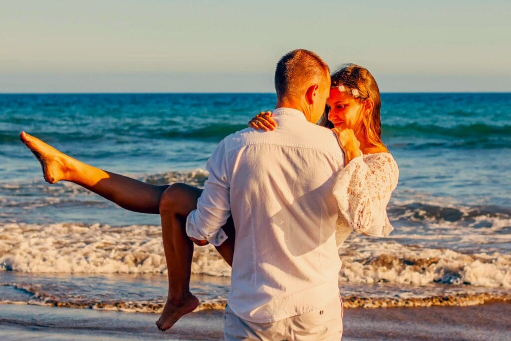 A man lifting his bride at the beach.